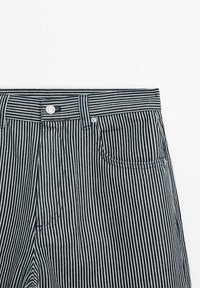 Gros plan sur un pantalon à rayures verticales bleu marine et blanches avec bouton frontal, passants pour ceinture et une poche avant sur fond blanc.