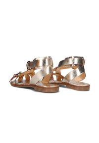 Metaalachtige gouden sandalen hebben meerdere riemen, een gespsluiting en een vlakke zool. Het ontwerp heeft een gladde textuur en minimale accenten.