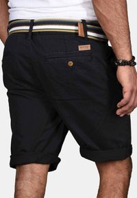 Black shorts made from lightweight fabric, featuring rolled cuffs, two back pockets with buttons, and a multi-striped woven belt.