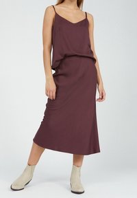 Viininpunainen hihaton mekko, jossa on rento malli ja midi-pituus, yhdistettynä vaaleanbeigeihin nilkkureihin. Sujuva kangas, jossa on hieno laskeutuminen.