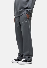 Grijze sweatpants van zacht materiaal, met een trekkoord in de taille, zakken en een bedrukt logo-detail. Gecombineerd met zwart-witte sneakers.