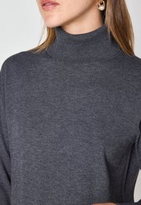 Maglione grigio a collo alto con una texture a coste, dall'elegante design aderente e senza chiusure o motivi visibili.