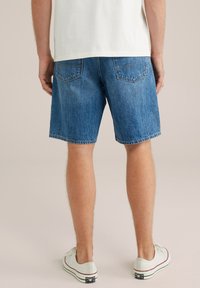 Traper šorts u svijetloplavoj boji s ravnim krojem, dva stražnja džepa i prošivenim rubom. Noseni s bijelim platnenim tenisicama.