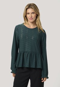 Türkises Langarm-Top mit Peplum-Design, ausgestattet mit einem gemusterten Stoff und gerafften Ärmeln, aus einem leichten, atmungsaktiven Material gefertigt.