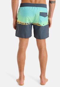 Męskie szorty kąpielowe w gradientowych odcieniach aqua i ciemnego niebieskiego. Posiadają elastyczny pas, tylną kieszeń z klapką oraz żółty pasek z logo.