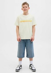 Light yellow cotton t-shirt with "project care" graphic in orange, paired with blue denim shorts and black-and-white sneakers.