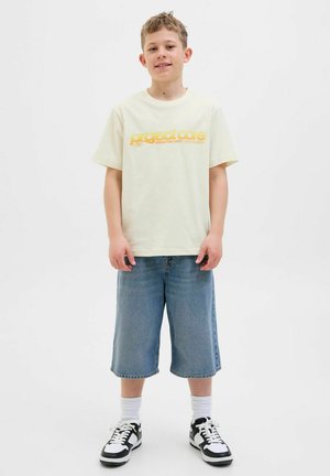 Light yellow cotton t-shirt with "project care" graphic in orange, paired with blue denim shorts and black-and-white sneakers.