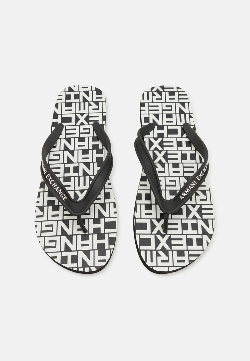 Svarte og hvite flip-flopper med et gjentagende tekstmønster og svarte gummistropper med "Armani Exchange"-merke. Flat såledesign.