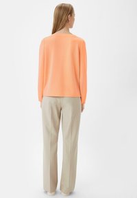 Langsleeve top in feloranje, met een ronde halslijn en een gladde textuur, gecombineerd met lichtbeige rechte broek.