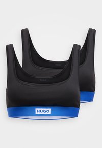 Kaksi mustaa urheiluliivejä leveillä olkaimilla ja sinisellä elastisella nauhalla, jossa on "HUGO"-logo. Sileä kangas, minimalistinen muotoilu.
