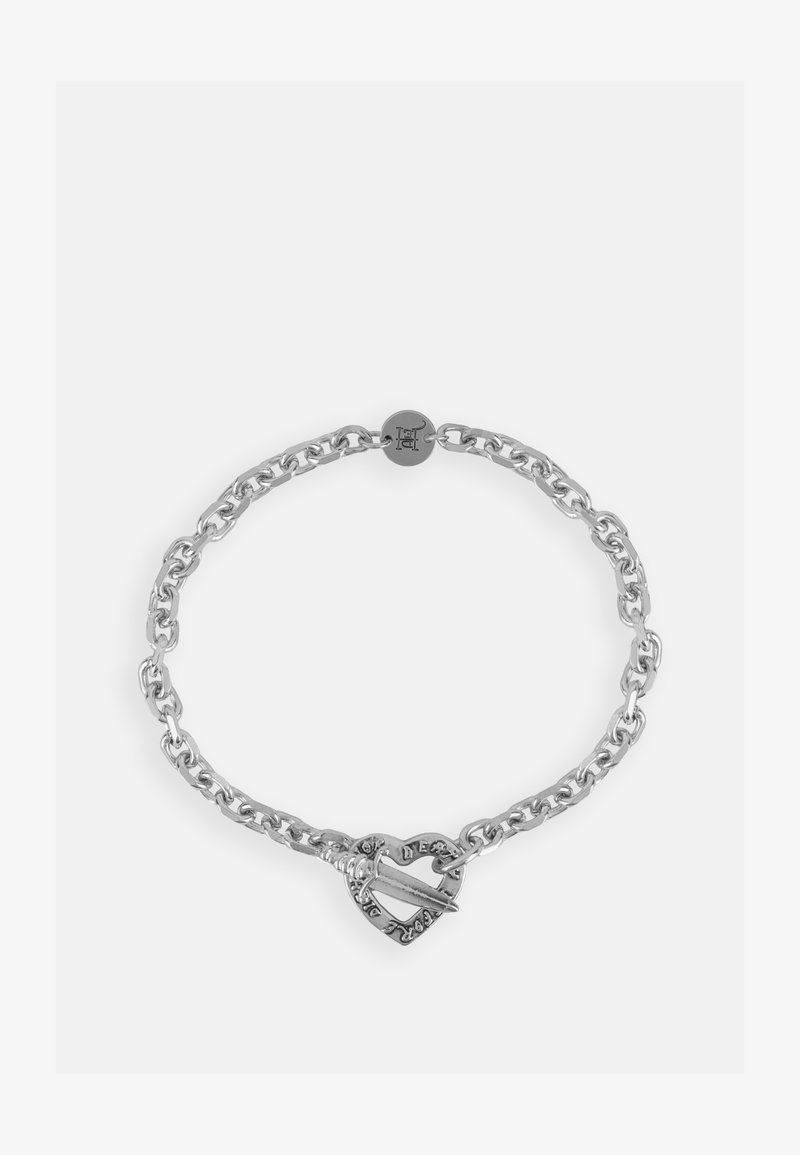 Zilveren schakelsieraden met een hartvormige sluiting met een haak en decoratieve elementen. De schakels zijn dik en gepolijst voor een glanzende afwerking.