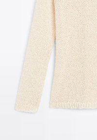 Sweter dzianinowy w kolorze jasnobeżowym z luźnym, teksturowanym splotem. Posiada długie rękawy i ściągacz na dole. Idealny do noszenia w warunkach chłodnych.