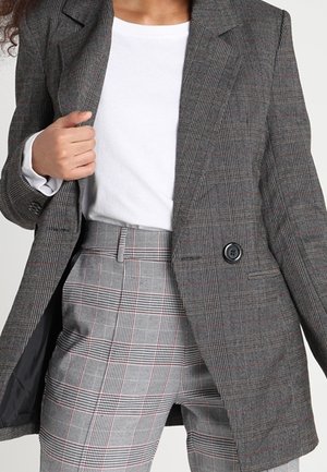 Grijze geruite blazer met een enkele knoopsluiting, gesneden revers en twee voorzakken, gecombineerd met lichtgrijze geruite pantalon.