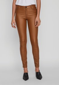 Hnědé slim-fit kalhoty vyrobené z hladkého, lesklého materiálu. Mají přední zapínání na knoflík a zip, s kapsami navrženými pro elegantní vzhled.