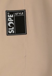Tessuto beige con una texture liscia, caratterizzato da un'etichetta rettangolare nera con la scritta bianca "SLOPE" e "STYLE" in lettere grasse.