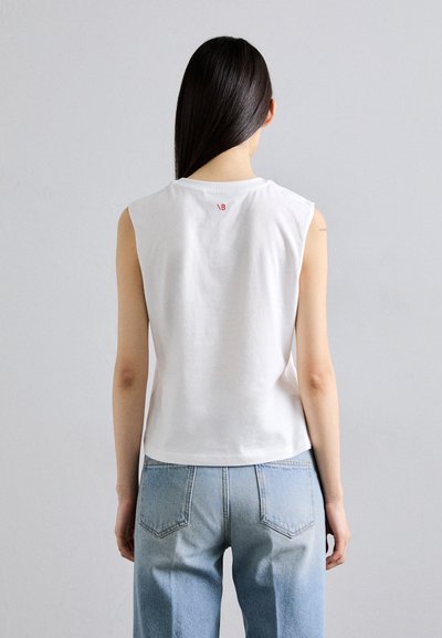 Weißes ärmelloses Oberteil aus Baumwolle mit Rundhalsausschnitt und kleinem roten Logo auf der Rückseite, getragen mit hellblauen hochgeschnittenen Jeans.