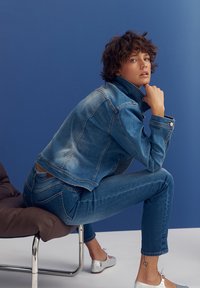 Blue denim jacket with a faded effect, paired with matching skinny jeans. Features a high collar and stitched detailing. Silver ballet flats.