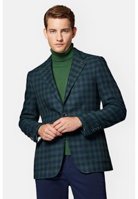 Ciemnozielona i granatowa marynarka w kratę z wyjściowym kołnierzem, pojedynczym zapięciem na guzik i srebrnymi elementami. Nałożona na dopasowany zielony golf.