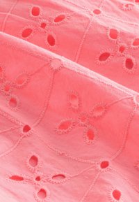 Korallfärgad bomullstyg med blommönster i brodyr och utskärningar. Texturerad yta med kontrasterande trådar som omger designen.
