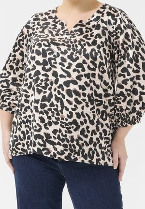 Kvinde iført en løs bluse med trekvartærmer med sort og beige leopardprint og mørkeblå jeans.