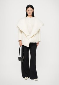 Bijela oversized puf jakna s velikim ovratnikom, uparena s kremastim topom, crnim rebrastim hlačama i malom crnom torbicom.