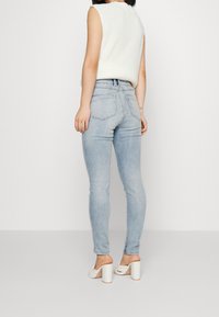 Vaaleansiniset skinny-farkut, joissa on korkea vyötärö, takataskut ja sileä farkutekstuuri. Yhdistetty valkoisiin korkokenkiin.