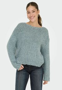 Losse trui van zacht, lichtblauw breiwerk met een geribbelde zoom en wijde mouwen, gecombineerd met donkere jeans. Gelaagd, chunky garen.