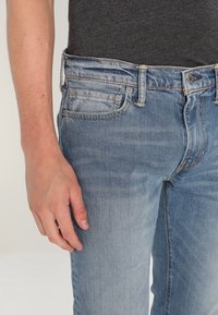 Bleka blå denimjeans med slim fit, med en femfickdesign, metallknap stängning och subtila slitningar.