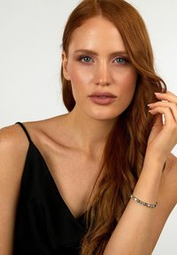 Bracciale d'argento con pietre blu e trasparenti, indossato su un polso. Chi lo indossa ha lunghi capelli rossi ed è vestita con un top nero senza maniche.