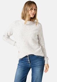 Pull en maille côtelée gris clair avec un col montant, agrémenté de subtils éclats ; associé à un jeans bleu avec des accents de boutons visibles sur le devant.