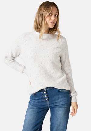 Pull en maille côtelée gris clair avec un col montant, agrémenté de subtils éclats ; associé à un jeans bleu avec des accents de boutons visibles sur le devant.