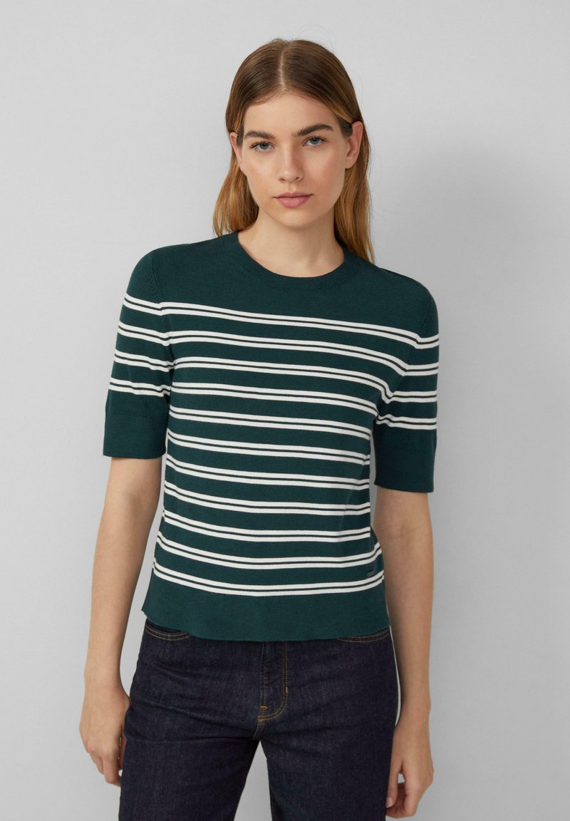 Grüner kurzärmeliger Pullover mit weißen horizontalen Streifen, geripptem Rundhalsausschnitt und cropped Schnitt, getragen mit dunklen Jeans.