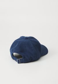 Navy corduroy pet met een gebogen rand, verstelbare achterkant en zichtbare stiksels. Getextureerde stof met ribbels voegt diepte toe.