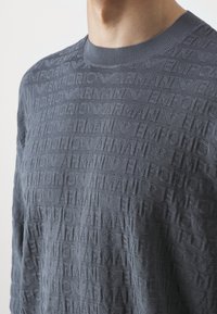 Szary sweter z długim rękawem wykonany z teksturowanego splotu z powtarzającym się logo "Emporio Armani", okrągłym dekoltem i fasonem o regularnym kroju.
