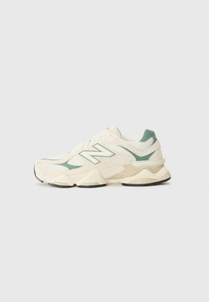 Kreemja ja piparmündi värvi New Balance'i tennisekad, millel on võrku ja sünteetilisi katteid, paks tall, ümmargune nina ja silmapaistvad brändimärgid küljel.