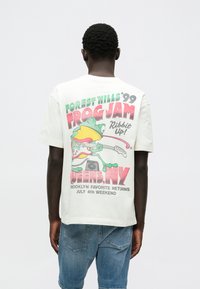 Λευκό βαμβακερό T-shirt με πολύχρωμο γραφικό βάτραχο που κρατάει κιθάρα, κείμενο "FOREST HILLS '99 FROG JAM" και στρογγυλή λαιμόκοψη.