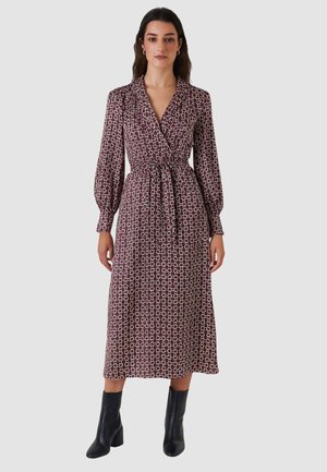 Abito lungo avvolgente color marrone scuro con motivo geometrico. Caratterizzato da scollo con colletto, vita annodata e maniche lunghe voluminose. Indossato con stivaletti neri alla caviglia.