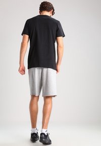 Camiseta negra de manga corta combinada con pantalones cortos deportivos grises. El conjunto presenta un ajuste relajado, material de algodón y es adecuado para un uso casual.