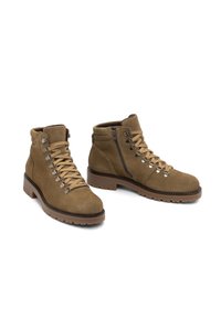 Botas de ante marrón hasta el tobillo con punta redonda, cierre de cordones y cremallera, acentos de herrajes metálicos y una suela de goma gruesa para tracción.