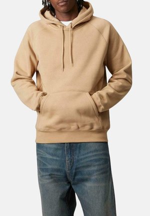 Sudadera beige con capucha con cordón, bolsillo tipo canguro y puños acanalados. Combinada con jeans azul, que presentan un corte relajado y una textura sutil.