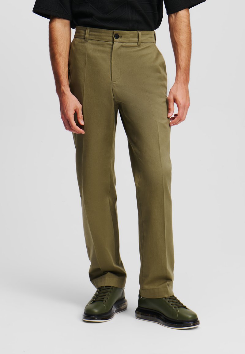 Pantaloni verde oliva realizzati in tessuto morbido, con una vestibilità dritta, tasche laterali e chiusura con un solo bottone. Abbinati a scarpe verde scuro.