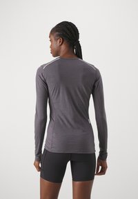 Long-sleeve athletic shirt in dark gray, made of stretchy fabric, featuring flat seams and a round neckline, paired with black shorts.