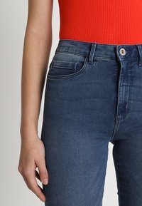 Blue denim jeans with a high-waisted design, featuring front pockets and a button closure. Smooth texture with a faded pattern.