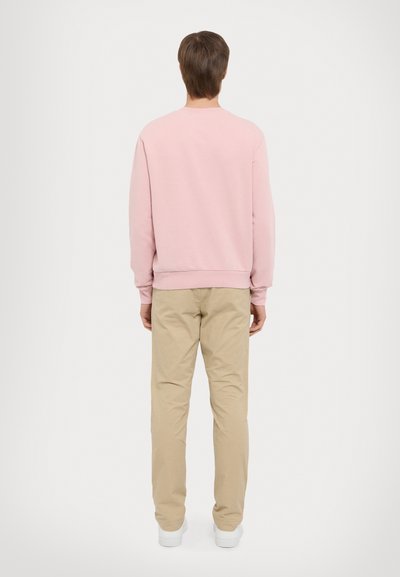 Rosa genser med lange ermer, ribbestrikkede mansjetter og mansjett. Kombinert med beige bukser og hvite joggesko. Enkelt, uformelt design.