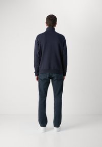 Pulover navy cu guler înalt, manșete și tiv ribbate, asortat cu blugi închiși și adidași albi. Design simplu, casual, fără modele.