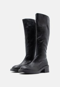 Μαύρες δερμάτινες μπότες μέχρι το γόνατο με λεία υφή, διακοσμημένες με φερμουάρ στο πλάι, στιβαρό τακούνι μπλοκ και στρογγυλεμένη μύτη.