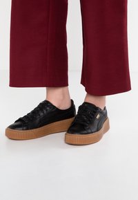 Sneaker nere in pelle con punta arrotondata, suola in gomma spessa e lacci piatti. Accenti testurizzati sui lati, branding minimale in oro.