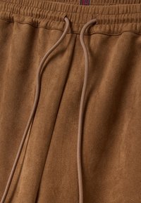 Pantalon en polaire marron avec taille élastique et cordons beiges noués légèrement à l'avant.