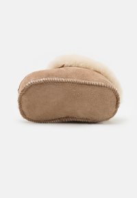 Brun mockasin av mocka med mjukt fuskpälsfoder, texturerad ovandel, rund tå och sydda detaljer runt sulan.