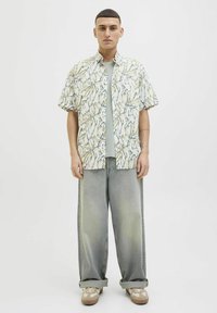 Kortærmet skjorte med knaplukning i gul og blå bananprint, parret med lysegrå wide-leg jeans og beige sneakers.